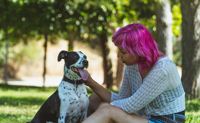 MUJER FELIZ AGARRANDO A  SU PERRO CON AMBAS MANOS EN EL PARQUE, NIÑA DE PELO ROSA MIRANDO A SU...