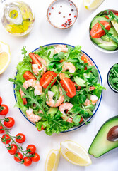 Shrimp salad with cherry tomatoes, arugula, avocado, and oil lemon dressing on white background. Top view