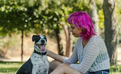 MUJER FELIZ AGARRANDO A  SU PERRO CON AMBAS MANOS EN EL PARQUE, NIÑA DE PELO ROSA MIRANDO A SU...