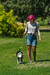 Mujer de pelo rosa paseando a su perro por el césped, perro blanco con manchas negras con su dueño en el parque, perro atado con correa en un paseo por el campo, adiestrando a un perro 