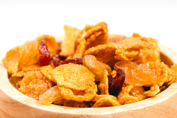 The wooden bowl of caramel cornflakes with raisins on white background for healthy eating and breakfast concept