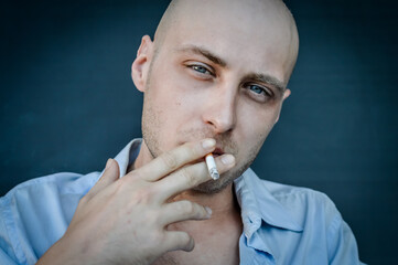 portrait of a young bald man smoking a cigarette while relaxing and looking in front of him