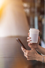 A businesswoman is drinking coffee and using a smartphone to communicate and check work from home online because she is starting a business that can order and check from anywhere online.