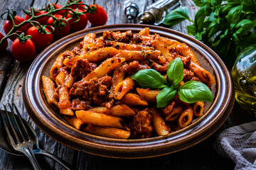 Penne with minced meat, tomato sauce, parmesan cheese, basil and vegetables served on wooden table 