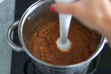Female hand mixes and makes fig jam in a pot on the stove at home in the kitchen. Close up, selective focus and copy space