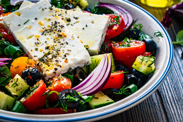Fresh Greek salad - feta cheese, cherry tomatoes, cucumber, black olives and onion on wooden table
