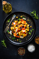 Gnocchi puttanesca - gnocchi with tomato sauce, anchovies, chili, capers and olives on wooden black table
