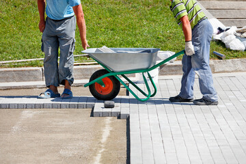 Workers carry paving slabs on a construction wheelbarrow to a work place for laying a pedestrian sidewalk.