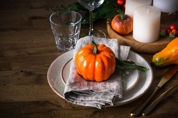 Autumn table setting with plate, pumpkin and candles at wooden table. Thanksgiving food festive dinner concept.