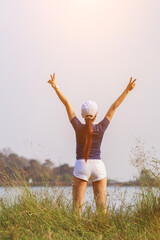 The girl raised her hands in the sky above the green meadow in the morning alone with happiness. The girl raised both hands to the sky to make a wish with faith and faith in the god.