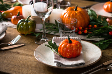 Autumn table setting with plate, glass, cutlery and autumn decor at wooden table. Thanksgiving food festive dinner concept.