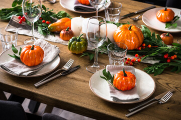 Autumn table setting with plate, glass, cutlery and autumn decor at wooden table. Thanksgiving food festive dinner concept.