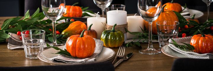 Autumn table setting with plate, glass, cutlery and autumn decor at wooden table. TLong banner format.