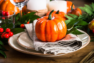 Autumn table setting with plate, pumpkin and candles at wooden table. Thanksgiving food festive dinner concept.