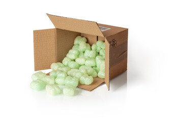 Shipping peanuts spilling out of the parcel box laying on its side, isolated on a white. Brown cardboard box with loose green foam fillers to protect fragile parcels in transit. Polystyrene pellets.