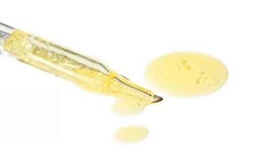 Liquid oil serum drop in pipette isolated on white background. Retinol, aha, bha acid, collagen skincare fluid, photo with shallow depth of field. Gold essence in dropper for beauty treatment