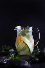 Homemade cold lemonade based on cucumber, mint and orange. Fresh fruit in a misted glass jug. Black background. Vertical photo.Copy space