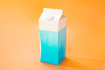 White and blue paper package of milk stands on orange background. Nutrition. Closed plastic cap....