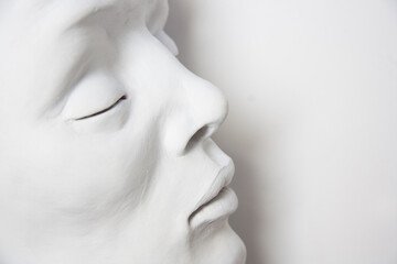 Portrait of a white face on a white background. Detail of sculpture with closed eyes.