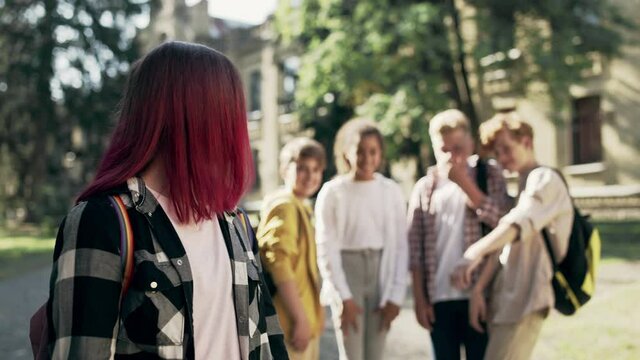 Group of school children bullying sad unpopular girl for distinctive appearance