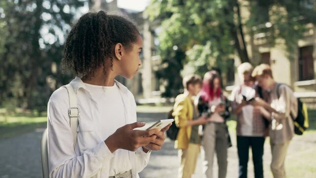 Sad biracial girl suffering social media bullying from group of school children