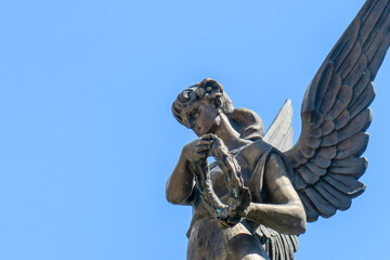 Sculpture of an angel with a wreath on a background of blue sky