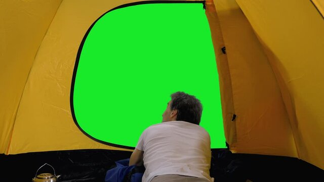 Rear view of man hiker lying inside tent and looking out on green screen background, chroma key 4k footage