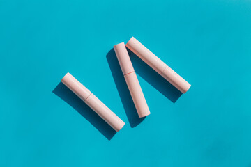 pink tubes of cosmetics on a blue background. Copy space. Closed tubes of lipstick, liquid lip...