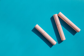 pink tubes of cosmetics on a blue background. Copy space. Closed tubes of lipstick, liquid lip...