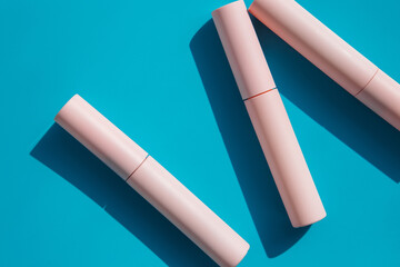 pink tubes of cosmetics on a blue background. Copy space. Closed tubes of lipstick, liquid lip gloss, mascara, eyeliner