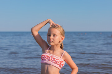 portrait of a girl 6-7 years old, blonde, standing in a swimsuit against the background of the sea