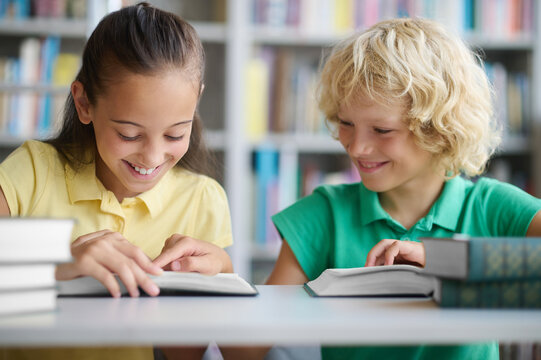 Two joyful classmates studying together at a public library