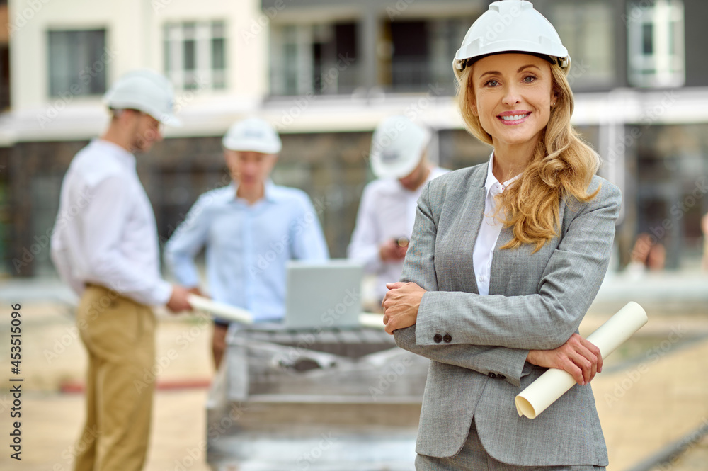 Poster Joyous determined female construction manager in a hardhat standing outdoors