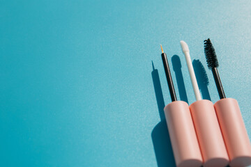 pink brushes for cosmetics, mascara, liquid lipstick, eyeliner, lip gloss on a blue background, copy space