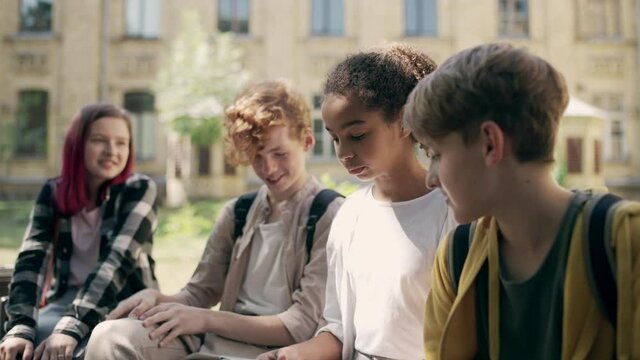 Happy multiethnic school friends talking and laughing during break, having fun