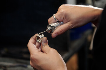 Close-up of unrecognizable manufacturing jeweler using polishing cone mounted on flex shaft while cleaning silver ring
