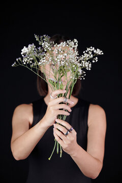 Woman in silver rings holding flowers against face while presenting new collection of jewelry, black background
