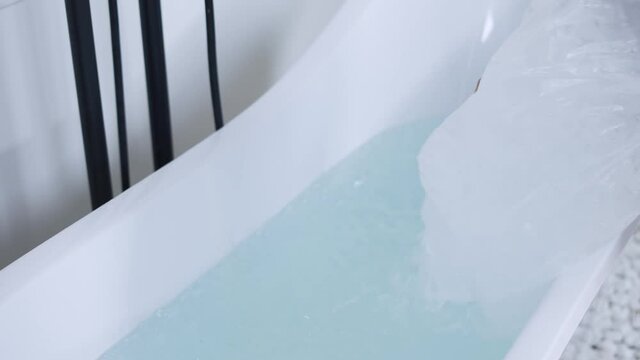 Unrecognizable man filling bath with ice cubes, close up