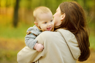 Obraz premium Cute little baby boy in his mothers arms. Mom and son having fun on sunny autumn day in city park. Son being held by his mommy.