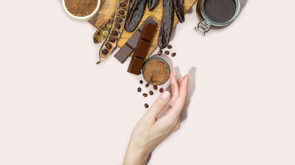 Organic carob pods, powder, chocolate and carob molasses on a wooden board in a woman hand on a...