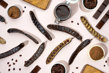 Organic carob pods, powder and carob molasses on a beige background, locust bean healthy food, Ceratonia siliqua harnup. Natural vegan eating. Creative food pattrern. Flat lay. Top view - obrazy, fototapety, plakaty