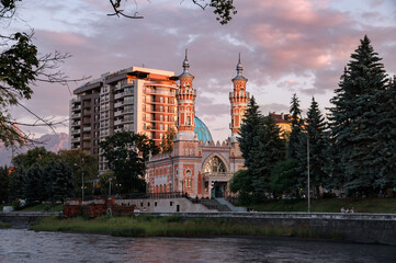 Obraz premium Minarets of Sunni Mukhtarov Mosque lit with warm sunset rays in front of pink gray clouds of summer evening sky on the bank of Terek river in Vladikavkaz city, North Ossetia Alania, Russia