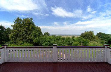 View from the balcony of a wooden old house on a summer green garden on a clear day. White railings. Red floor.