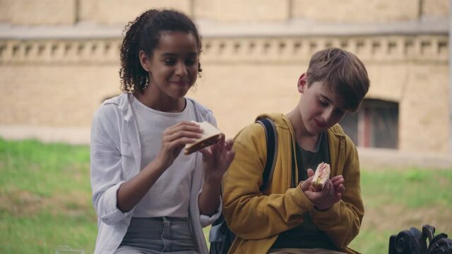 Multicultural school friends eating sandwiches during break, having fun together