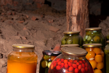 Glass jars with canned vegetables, fruits and berries are in the village cellar. Close-up. Old banks.. The foreground is a yellow and red jar. - obrazy, fototapety, plakaty