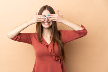 Young caucasian woman isolated on beige background covering eyes by hands and smiling