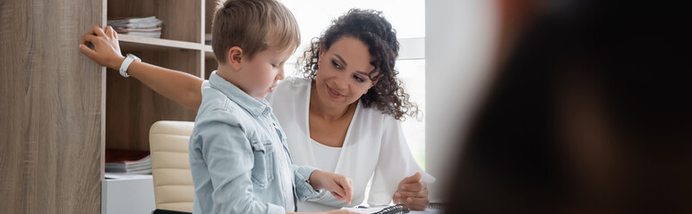 positive african american teacher talking to schoolboy in classroom, banner