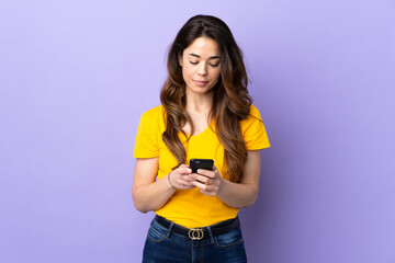 Woman over isolated purple background sending a message with the mobile