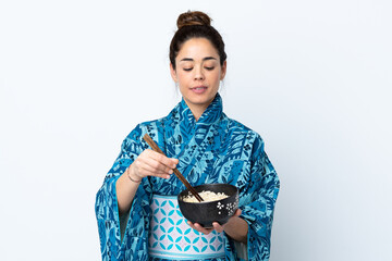 Woman wearing kimono over isolated white background holding a bowl of noodles with chopsticks