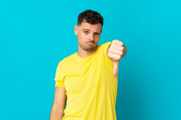 Young caucasian handsome man isolated on blue background showing thumb down with negative expression